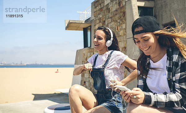 Zwei fröhliche junge Frauen  die Musik hören und Spaß am Strand haben.