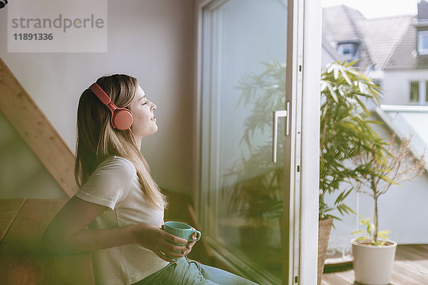 Junge Frau entspannt zu Hause bei einer Tasse Tee  Musik hören