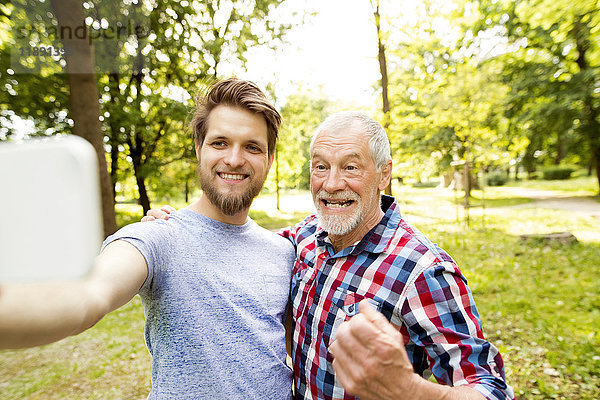 Porträt eines älteren Vaters und seines erwachsenen Sohnes  der sich in einem Park aufhält.