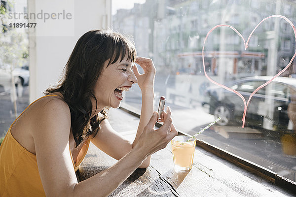 Frau im Café sitzend zeichnet Herzform auf Fensterscheibe mit Lippenstift