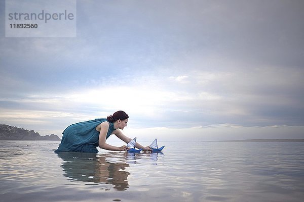 Frau mit blauen Papierschiffen bei Ebbe am Strand
