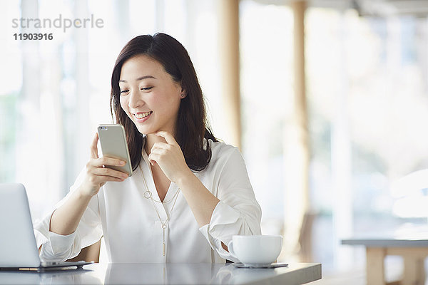 Japanische Frau mit Smartphone in einem schicken Cafe