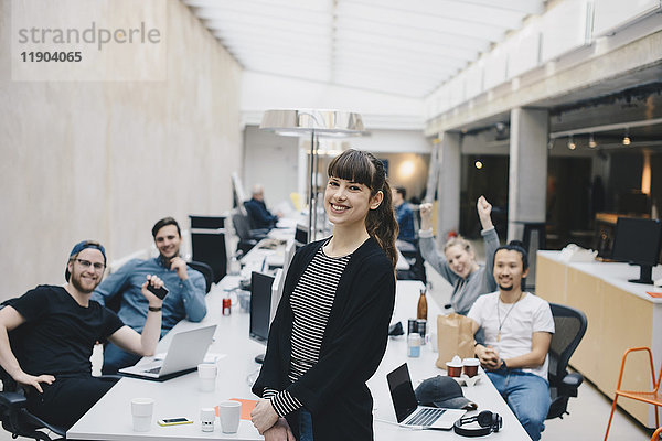 Porträt einer glücklichen Programmiererin mit Kollegen am Schreibtisch im Hintergrund