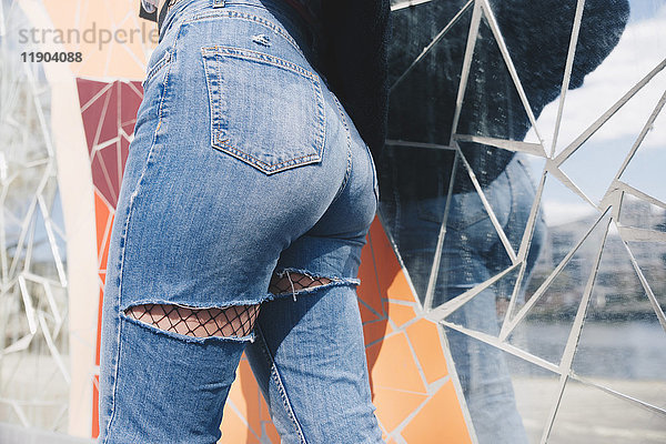 Mittelteil der jungen Frau in zerrissener Jeans gegen MosaikwandMittelteil der jungen Frau in zerrissener Jeans gegen mos