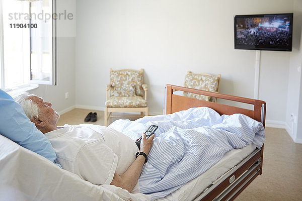 Älterer Mann beim Fernsehen auf dem Bett in der Krankenstation