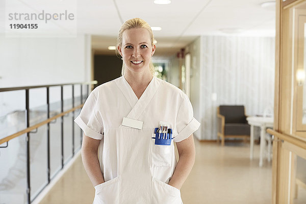 Porträt einer glücklichen Krankenschwester mit den Händen in den Taschen im Flur des Krankenhauses.