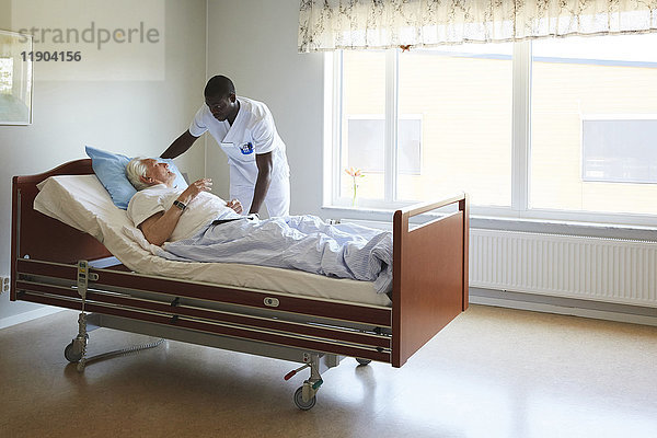 Krankenpfleger  der das Bett eines älteren Mannes in der Krankenstation anpasst.