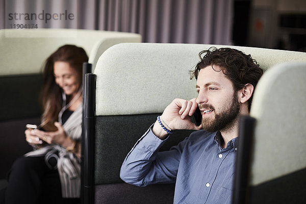 Lächelnde Geschäftskollegen mit Smartphones auf Stühlen im Kreativbüro
