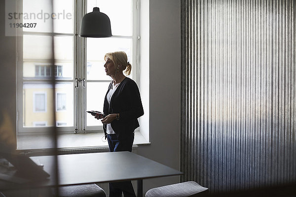 Senior Geschäftsfrau mit Handy gegen Fenster im Kreativbüro