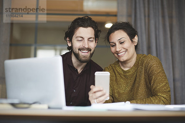 Lächelnde Geschäftskollegen mit dem Handy im Kreativbüro