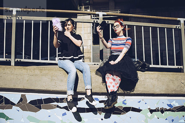 Hipster-Freundinnen nehmen Selfie mit dem Handy  während sie an der Wand gegen das Geländer sitzen.