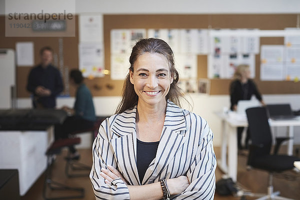 Porträt einer lächelnden Geschäftsfrau mit Kollegen im Hintergrund im Kreativbüro
