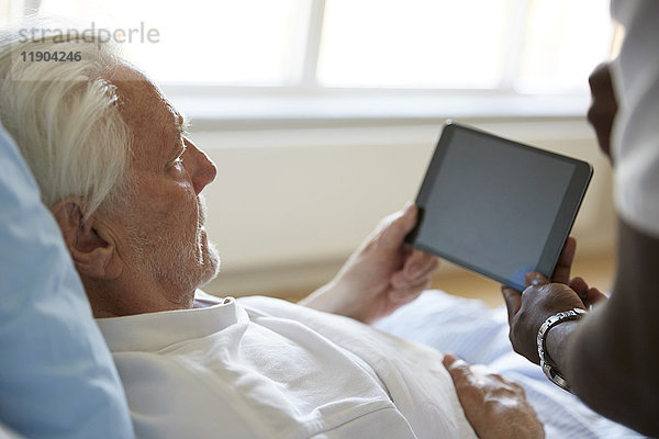Abgeschnittenes Bild eines Krankenpflegers  der den älteren Mann bei der Verwendung von digitalen Tabletten im Krankenhaus unterstützt.