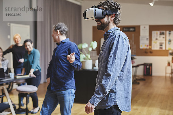 Geschäftsmann nutzt Virtual-Reality-Simulator  während er Kollegen im Kreativbüro zur Seite steht.