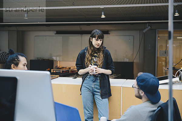 Computerprogrammiererin mit Kaffeetasse im Gespräch mit Kollegen im Büro