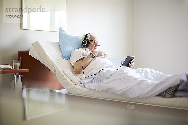 Älterer Mann mit digitalem Tablett auf dem Bett in der Krankenstation