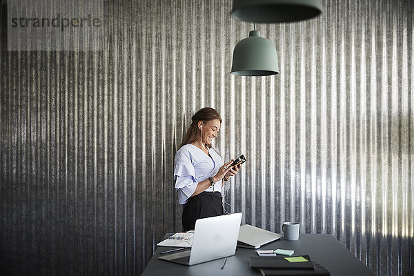 Lächelnde reife Geschäftsfrau mit dem Handy an der Wellblechwand im Kreativbüro