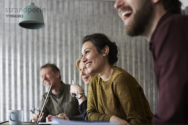 Fröhliche  kreative Geschäftskollegen sitzen am Konferenztisch und schauen weg in den Sitzungssaal.