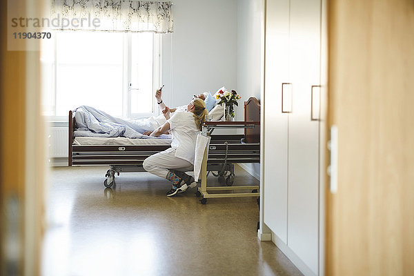 Krankenschwester und älterer Mann  der Selfie mit Smartphone in der Krankenstation nimmt