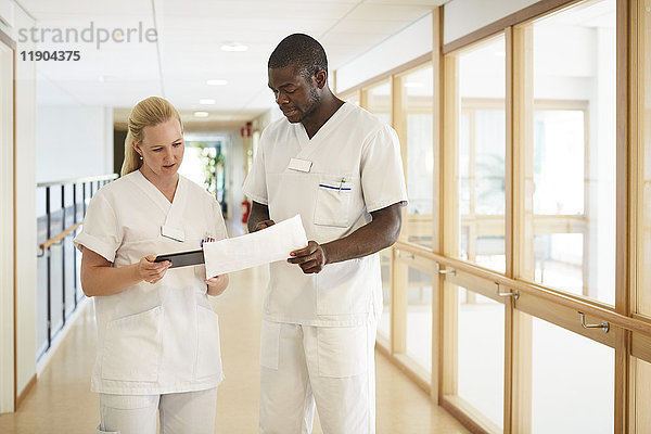 Krankenschwester und Krankenpflegerin mit digitalem Tablett bei der Untersuchung von Dokumenten im Krankenhauskorridor