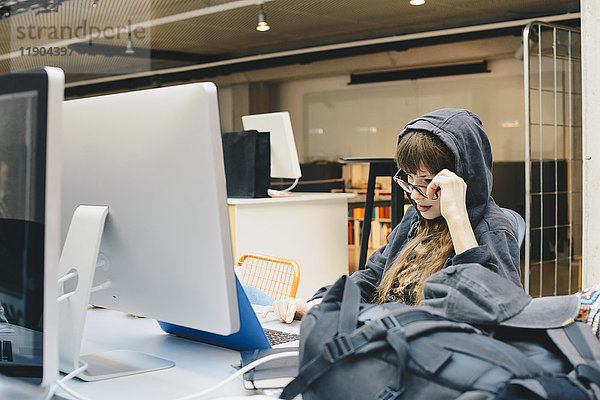 Weibliche Programmiererin mit Laptop beim Blick über die Brille im Büro