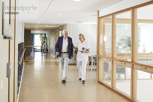 Volle Länge der Krankenschwester und des älteren männlichen Patienten  die im Krankenhausflur gehen.