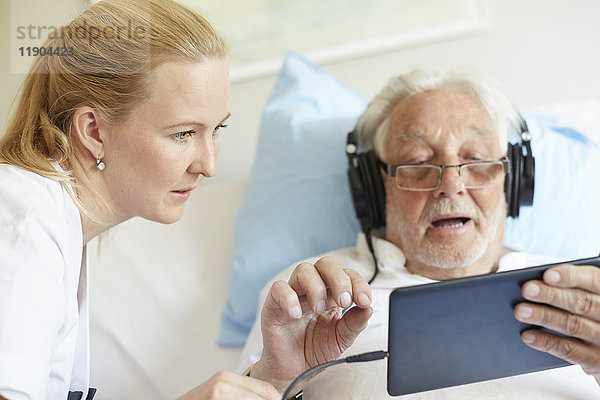 Krankenschwester unterstützt älteren Mann bei der Verwendung von digitalen Tabletten auf dem Krankenhausbett