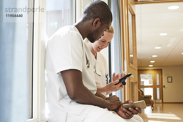 Multiethnische Krankenschwestern mit Smartphone auf der Fensterbank im Krankenhaus