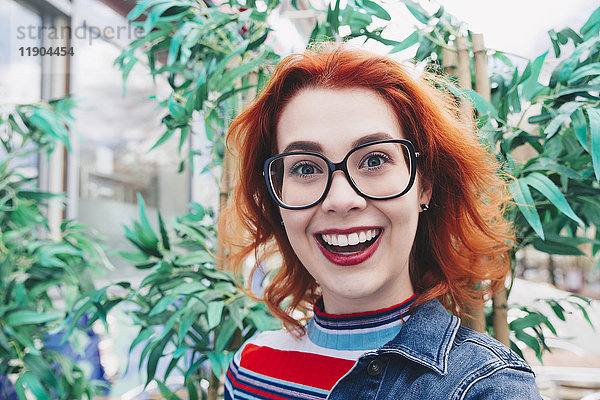 Porträt einer lächelnden rothaarigen jungen Frau gegen die Pflanze