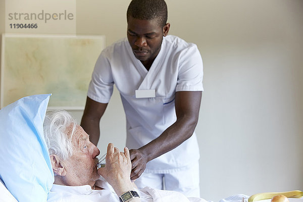 Krankenschwester füttert den älteren Mann auf der Krankenstation mit Wasser