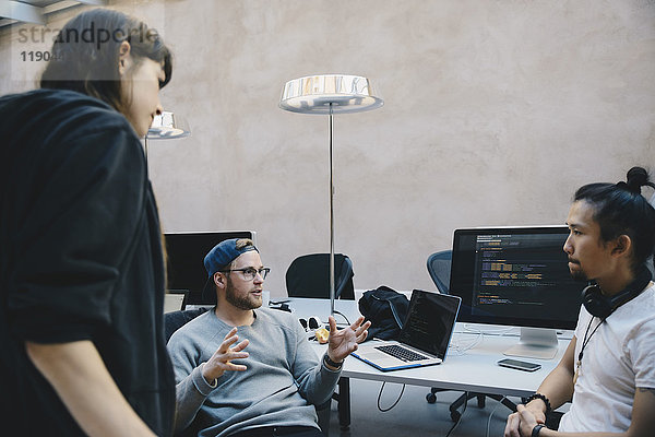 Computerprogrammierer gestikuliert  während er mit Kollegen im Kreativbüro über den Plan diskutiert.