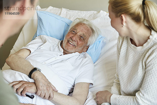 Glücklicher älterer Mann  der mit einem Paar spricht  während er auf dem Bett in der Krankenstation liegt.