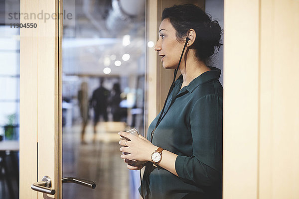 Seitenansicht der Geschäftsfrau mit Smartphone aus Glas im Büro gesehen