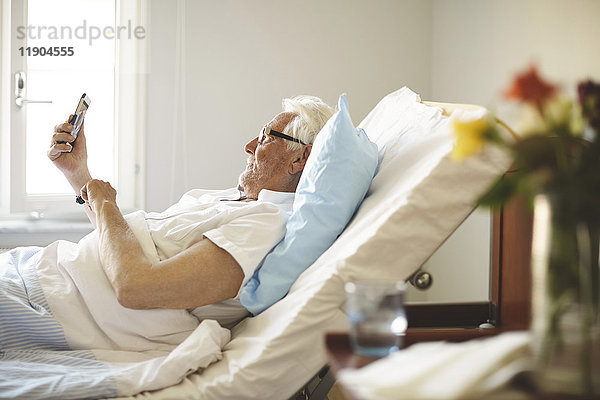 Senior Mann  der Selfie mit Smartphone auf dem Bett in der Krankenstation nimmt