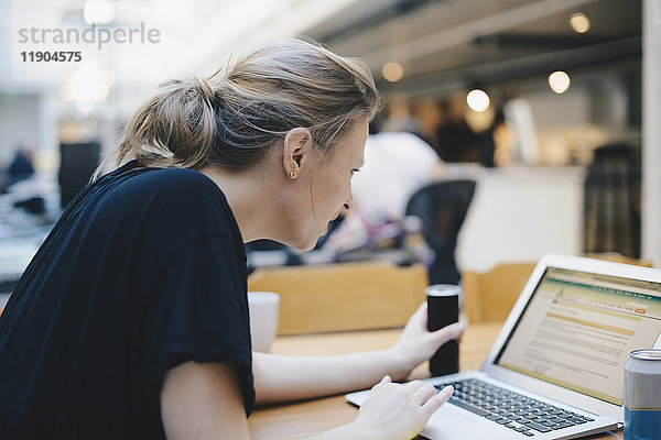 Seitenansicht der jungen Programmiererin mit Laptop am Schreibtisch im Büro