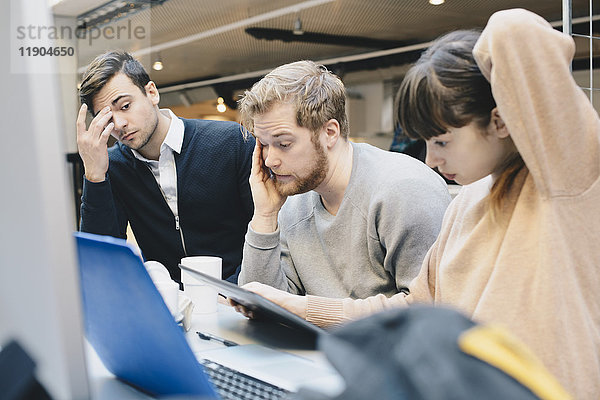 Gestresste Computerprogrammierer mit digitalem Tablett am Schreibtisch im Büro