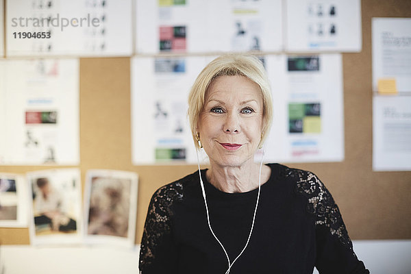Porträt einer lächelnden Seniorin mit Kopfhörer am schwarzen Brett im Kreativbüro