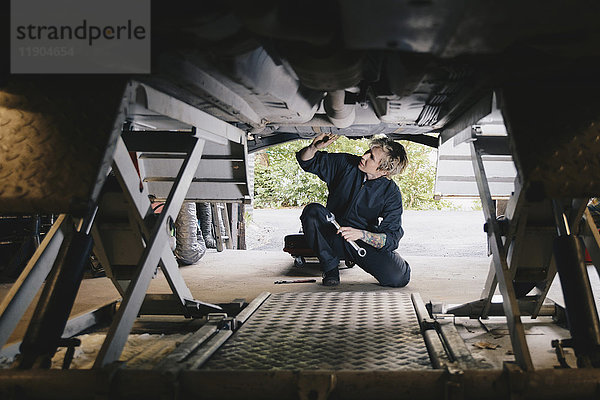 Kniende Mechanikerin bei der Untersuchung unter dem Auto in der Autowerkstatt
