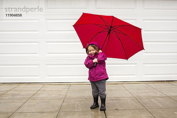 Kaukasisches Mädchen hält roten Regenschirm im Wind