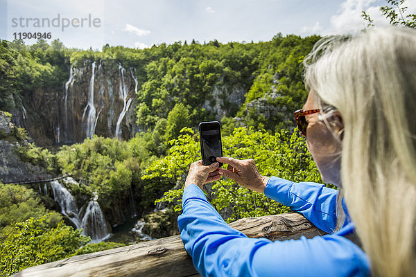 Ältere kaukasische Frau fotografiert Wasserfälle mit Handy