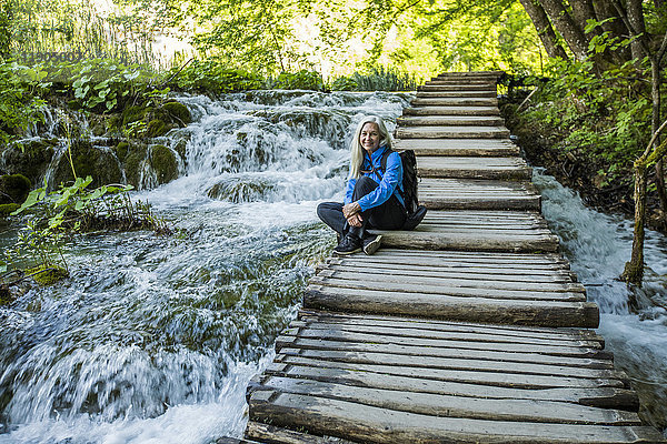 Ältere kaukasische Frau sitzt auf einer Holztreppe über einem Wasserfall