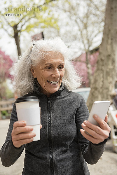 Ältere Frau trinkt Kaffee und schreibt eine SMS mit ihrem Handy