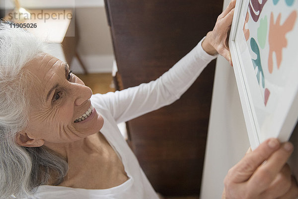 Ältere Frau hängt Kunstwerke an die Wand