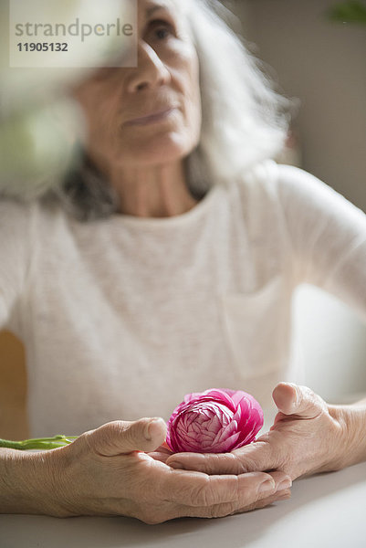 Ältere Frau hält rosa Blume