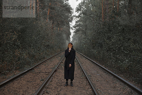 Kaukasische Frau hält Herbstblatt auf Bahngleisen im Wald