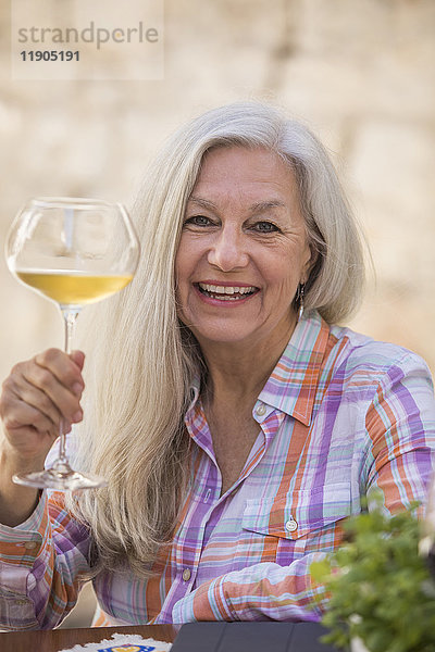 Lächelnde ältere kaukasische Frau mit Weißwein in der Hand