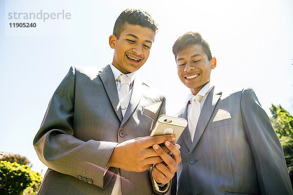 Hispanische Jungen in Anzügen  die mit ihrem Handy SMS schreiben