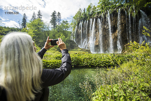 Ältere kaukasische Frau fotografiert Wasserfall mit Handy