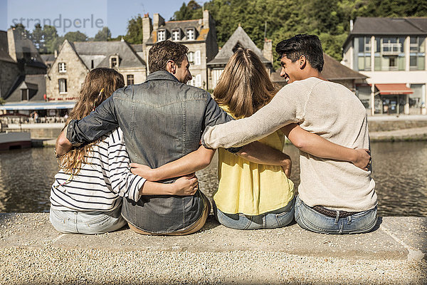 Freunde sitzen und umarmen sich am Wasser