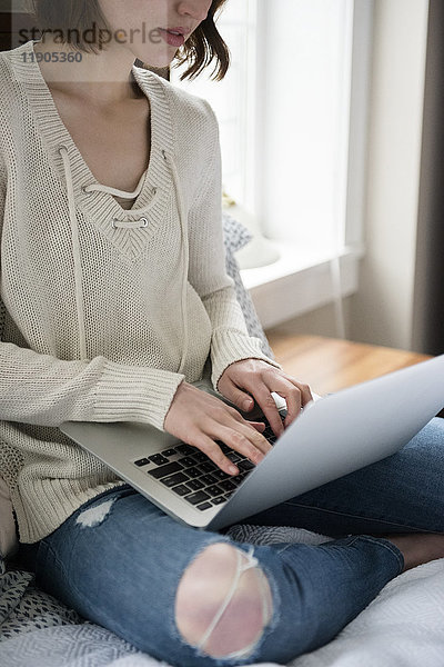 Kaukasische Frau sitzt auf dem Bett und benutzt einen Laptop